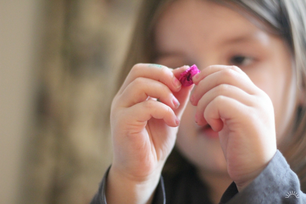 A little girl scrunching up tissue paper for an easy Valentines craft