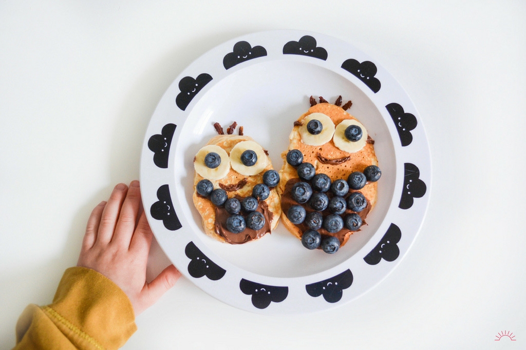 A child's hand next to a plate of Minion themed pancake art