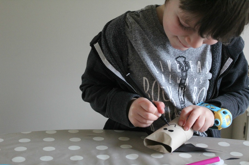 A boy drawing a face on his bat made out of toilet roll